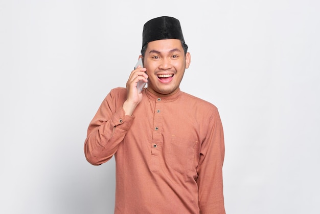 Wesoły młody azjatycki muzułmanin rozmawia przez telefon komórkowy na białym tle na białym tle