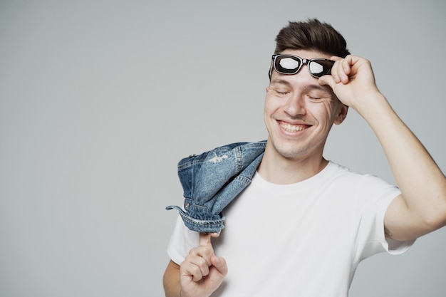 Wesoły młody człowiek trzymający okulary przeciwsłoneczne w dłoniach na twarzy uśmiechający się zabawny żart pokazuje