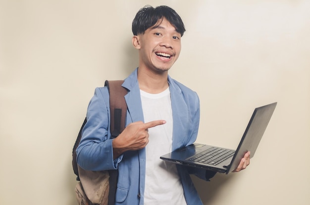 Wesoły młody człowiek ubrany w garnitur z college'u, niosąc laptopa i plecak na na białym tle