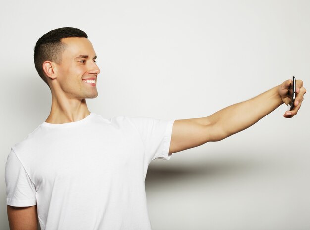 Zdjęcie wesoły młody człowiek w koszuli trzymający telefon komórkowy i robiący sobie zdjęcie