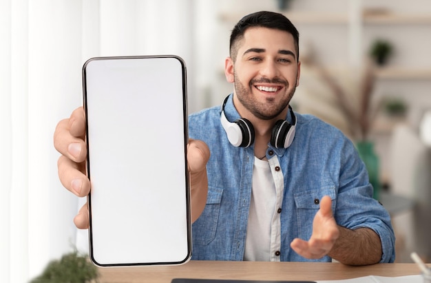 Wesoły młody facet pokazujący duży telefon komórkowy z pustym białym ekranem
