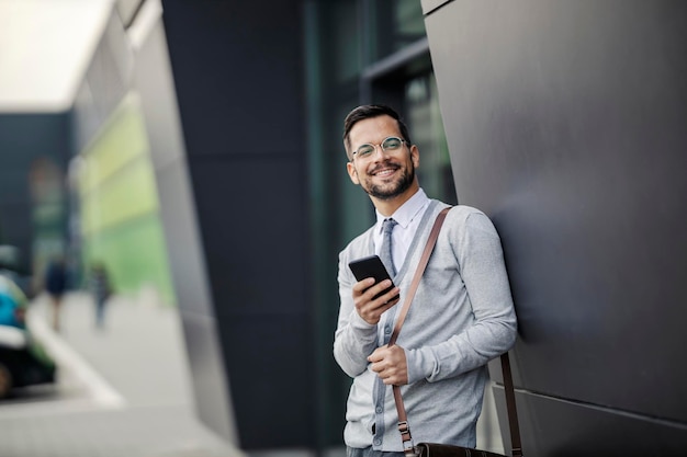 Wesoły, młody, inteligentny dyrektor stoi w centrum biznesowym i korzysta z telefonu