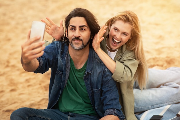 Wesoły młody mężczyzna i kobieta biorący selfie na smartfonie na zewnątrz i wygłupiający się