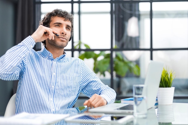 Wesoły młody operator telefonu obsługującego mężczyznę w zestawie słuchawkowym w miejscu pracy podczas korzystania z usługi pomocy komputerowej i koncepcji call center konsultacyjnej z klientem