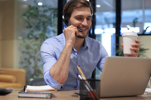 Wesoły Młody Wsparcie Telefon Mężczyzna Operatora W Zestawie Słuchawkowym, W Miejscu Pracy Podczas Korzystania Z Laptopa, Usługi Pomocy I Koncepcja Call Center Konsultacji Klienta.