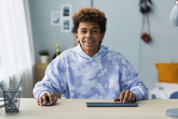 Wesoły nastoletni uczeń naciskając klawisze klawiatury komputera