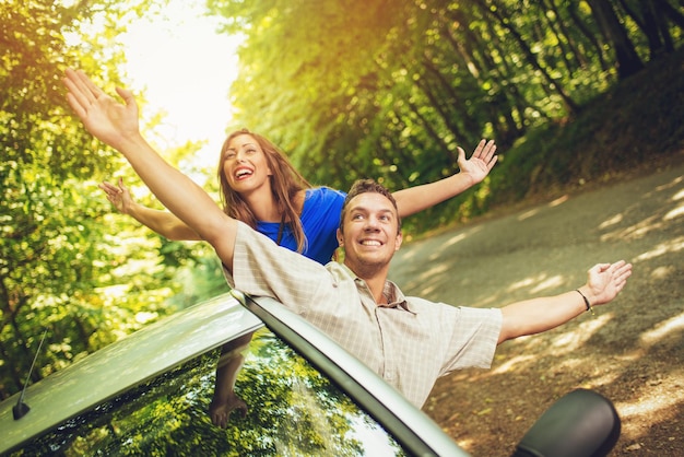 Wesoły podróżnicy na letnie wakacje wychylają się z okna samochodu z podniesionymi rękami.