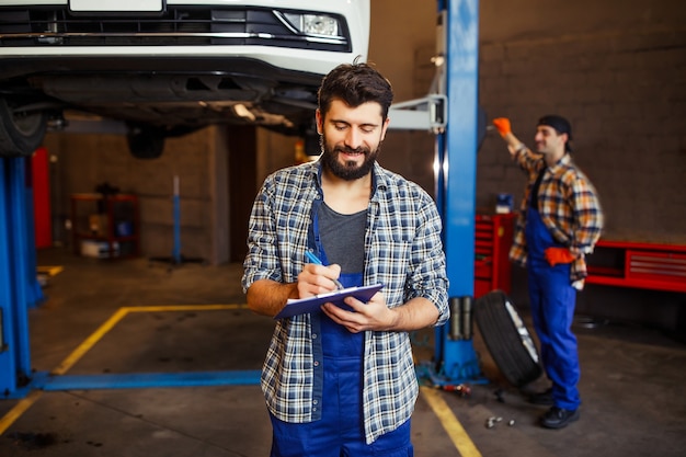 Wesoły Pracownik W Mundurze Robiący Notatki I Automechanik Za Wspólnym Budzeniem