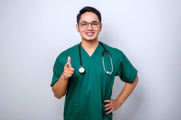 Wesoły przystojny azjatycki mężczyzna pielęgniarka lub lekarz w zielonym zarośla stetoskop wskazując aparat