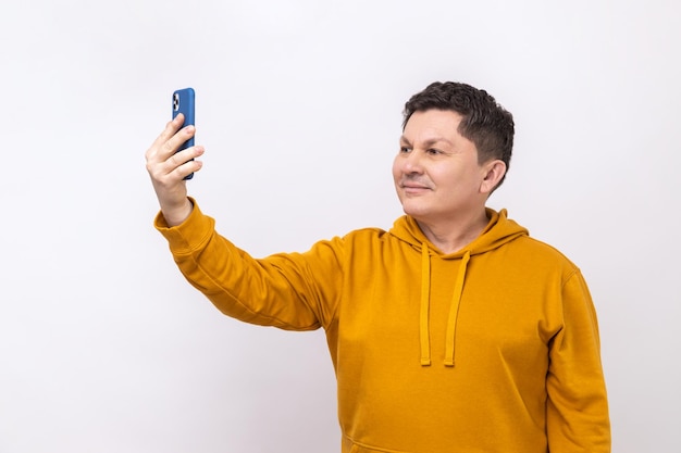 Wesoły, przystojny mężczyzna robi selfie za pomocą smartfona rozmawiając podczas wideorozmowy i uśmiechając się radośnie