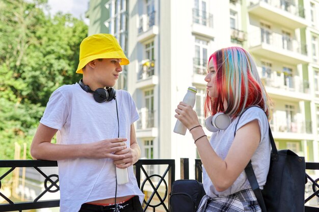 Zdjęcie wesoły rozmawiający studenci nastolatki facet i dziewczyna w mieście pijący jogurt mleczny z butelki styl życia odżywianie młodzież zdrowie