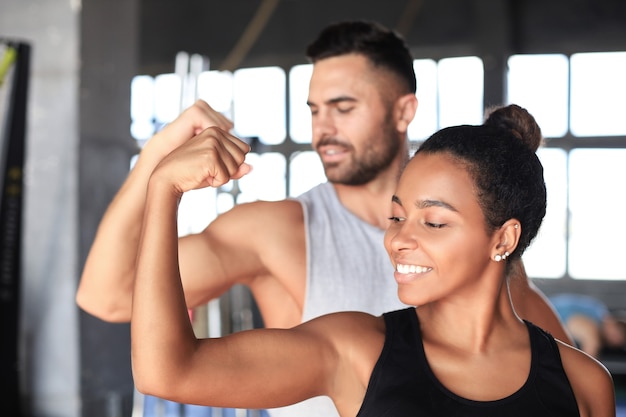 Wesoły sportive para razem trenuje i pokazuje bicepsy na siłowni.