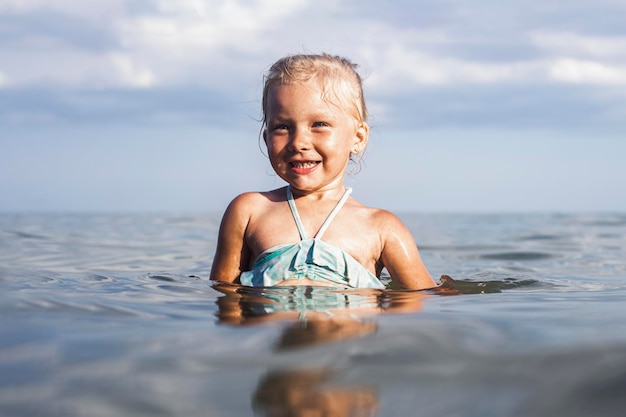 Wesoły uśmiechający się blond dziewczynka pływanie w morzu w letni dzień.