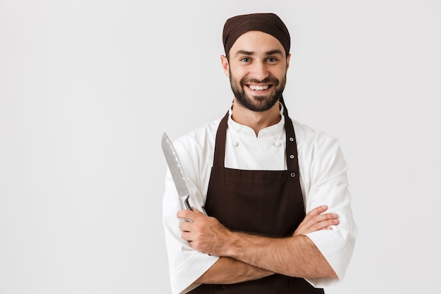 wesoły uśmiechający się optymistyczny młody sous-chef pozowanie w mundurze trzymając nóż.