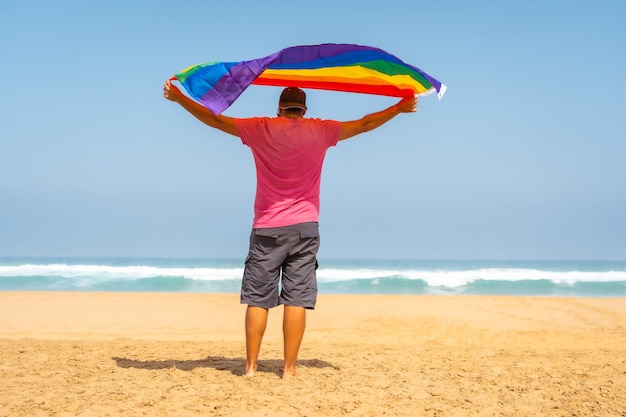 Wesoły W Różowej Koszulce I Czarnej Czapce Z Flagą Lgbt Na Plaży, Symbol Homoseksualizmu