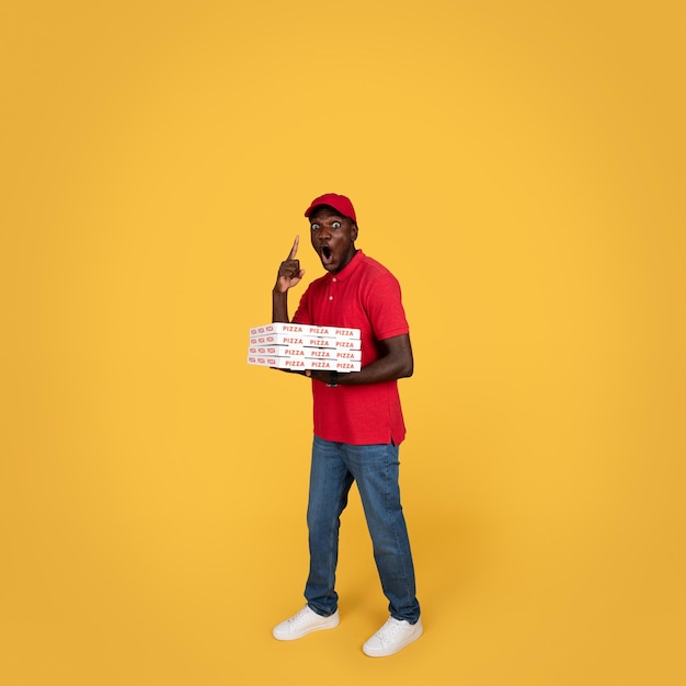 Wesoły, zszokowany, tysiącletni kurier, Afroamerykanin, z otwartymi ustami, trzyma wiele pudełek po pizzy