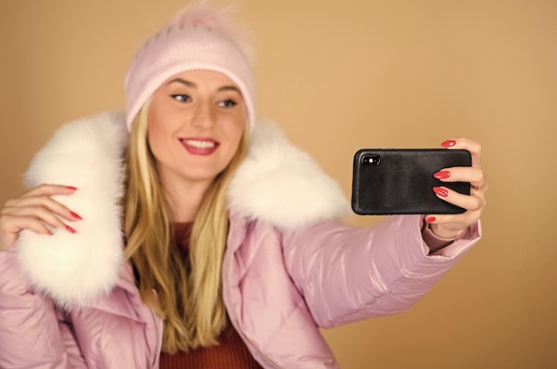 Wesołych ferii zimowych blogerka internetowa w bufiastym płaszczu robi selfie ze sztucznego futra moda ciepła zimowa odzież telefon selfie grypa i zimna pora roku Skórzana torba moda kobieta w czapce beanie