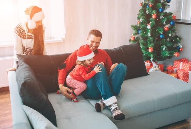 Wesołych Świąt i Szczęśliwego Nowego Roku. Rodzinny portret. Młody człowiek siedzi na kanapie z córką