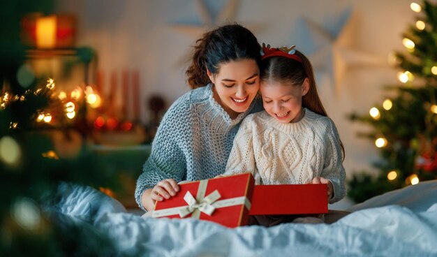 Zdjęcie wesołych świąt i szczęśliwych święt wesoła mama i jej urocza córka wymieniają się prezentami