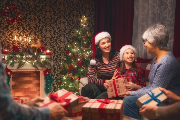 Wesołych Świąt i Wesołych Świąt! Babcia, dziadek, mama, tata i dziecko wymieniają się prezentami. Rodzice i córka zabawy w pobliżu drzewa w pomieszczeniu. Kochająca rodzina z prezentami w pokoju.