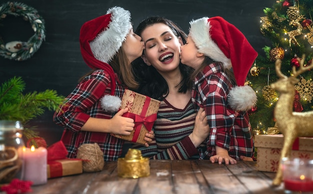 Wesołych Świąt i Wesołych Świąt! Mama i córki z prezentami w pobliżu drzewa w domu.