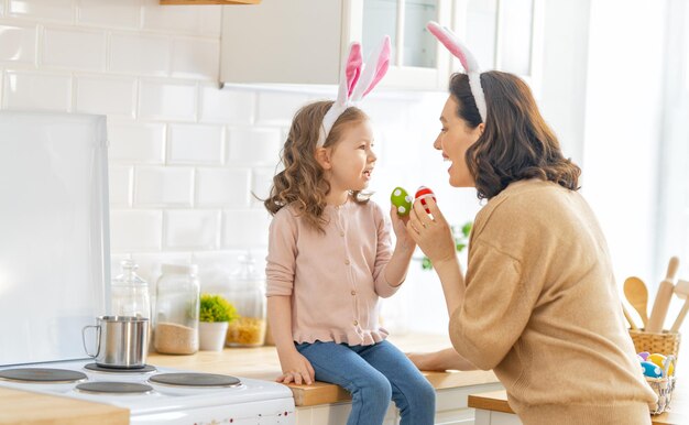 Wesołych Świąt! Matka z córką malują jajka. Rodzina przygotowuje się do Wielkanocy. Cute dziewczynka dziecko ma na sobie uszy królika.