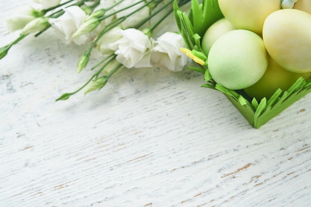 Wesołych Świąt Wielkanocnych jajka i królik w zielonym koszu na białym starym drewnianym stole z białymi i żółtymi różami Wiosna Wesołych Świąt Kartka świąteczna Tło wielkanocne z miejsca na kopię Widok z góry