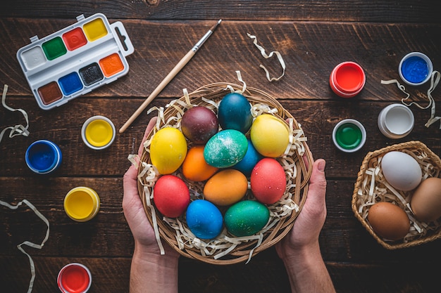 Wesołych Świąt Wielkanocnych. Malowanie i przygotowywanie kolorowych jaj na święta wielkanocne. Widok z góry. Barwioni jajka w koszu w rękach na drewnianym stole