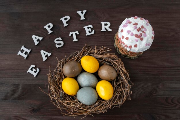 Wesołych Świąt Wielkanocnych Napis Wielkanocny Ciasto i Kolorowe Jaja w Ptasim gnieździe na drewnianym stole
