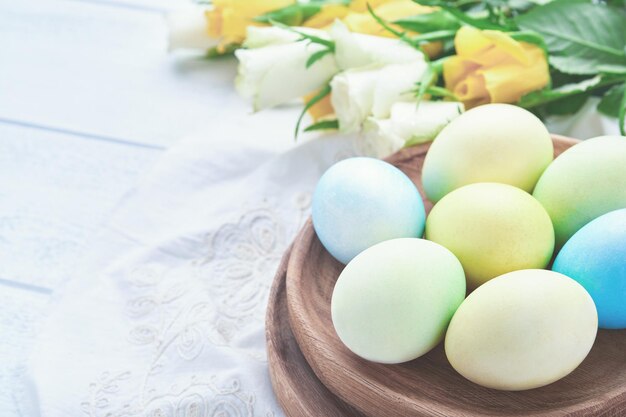 Wesołych Świąt Wielkanocnych pisanki na rustykalnym stole z białymi i żółtymi różami Naturalnie barwione kolorowe jajka w drewnianym talerzu i wiosenne kwiaty w rustykalnym pokoju Stonowany obraz Tło wielkanocne z miejsca na kopię
