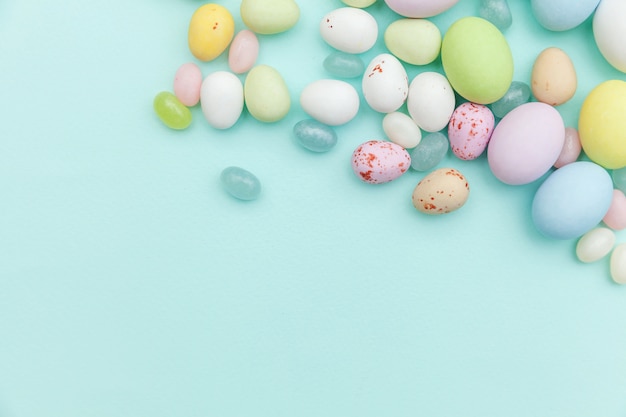 Wesołych Świąt Wielkanocnych. Przygotowanie do wakacji. Wielkanocne cukierki czekoladowe jajka i słodycze żelkowe na modnym pastelowym niebieskim tle. Widok z góry prosty minimalizm płasko widok z góry.