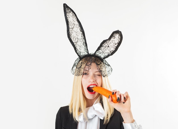Wesołych Świąt Wielkanocnych. Seksowny Zajączek jedzący marchewkę. Zmysłowa kobieta ubrana w czarne koronkowe uszy królika Wielkanoc