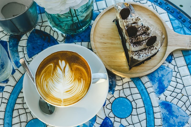 Wesołych świątGorąca kawa latte z pianką mleczną latte art w kubku i domowe ciasto czekoladowe z dekoracjami świątecznymi i bombkami choinkowymi na biurku z marmurową podłogą Świętując Wesołych Świąt i Nowego Roku