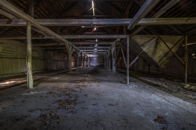 Zdjęcie wewnątrz ciemnego, opuszczonego, zrujnowanego drewnianego hangaru z gnijącymi kolumnami