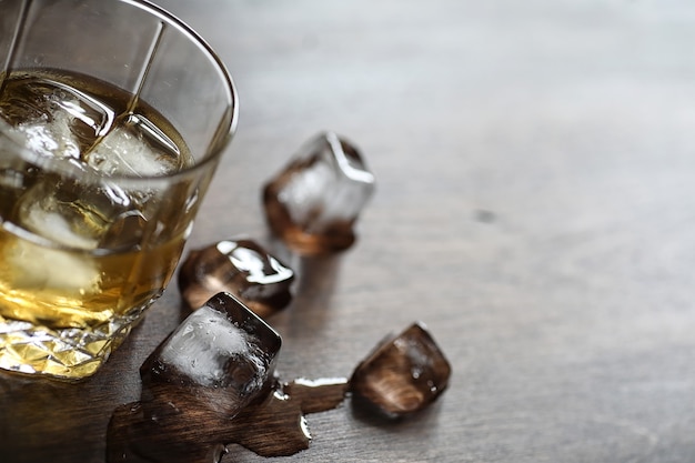 Whisky w szklance i kawałki lodu na drewnianym stole