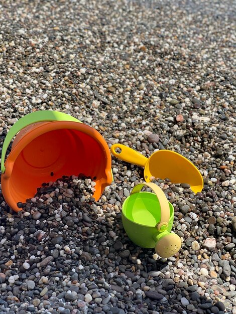 wiadro, konewka i łopata na kamienistej plaży, zabawki dla dzieci z jasnym piaskiem, zdjęcie na telefonie