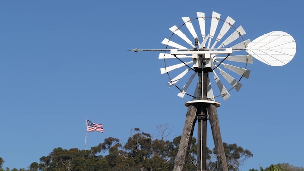 Wiatrak, łopatkowy Wirnik I Flaga Usa Przeciw Błękitne Niebo. Turbina Wiatrowa Z Pompą Wodną, Generator Prądu.