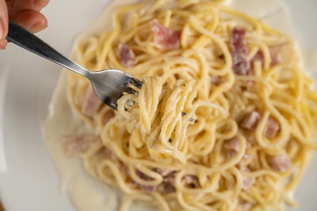 Widelec obraca spaghetti carbonara na białym talerzu