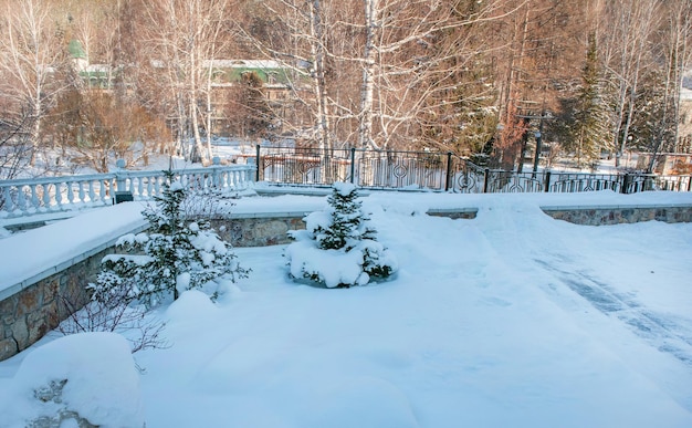Widoczny zaśnieżony park z kamienną balustradą i ogrodzeniem, przez który widać dom