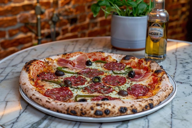 Widok boczny na pizzę z salami, szynką, zielonymi paprykami, pomidorami, czarnymi oliwkami i serem na stole