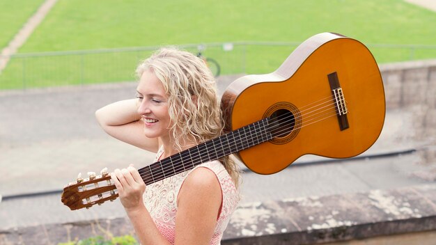 Zdjęcie widok boczny uśmiechniętej kobiety patrzącej w stronę, trzymając gitarę