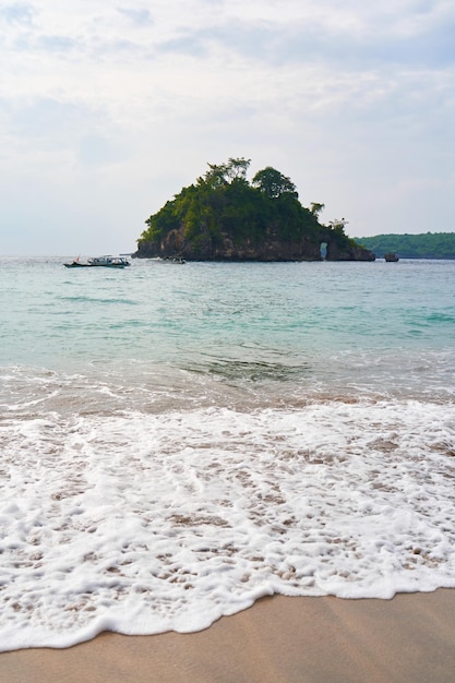 Zdjęcie widok burzliwego oceanu, który myje piaszczyste plaże falami, mała zielona wyspa w morzu.