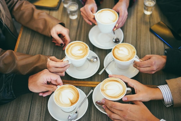 Widok dłoni ludzi pijących cappuccino w zabytkowej kawiarni. Skup się na lewej ręce mężczyzny trzymającego filiżankę