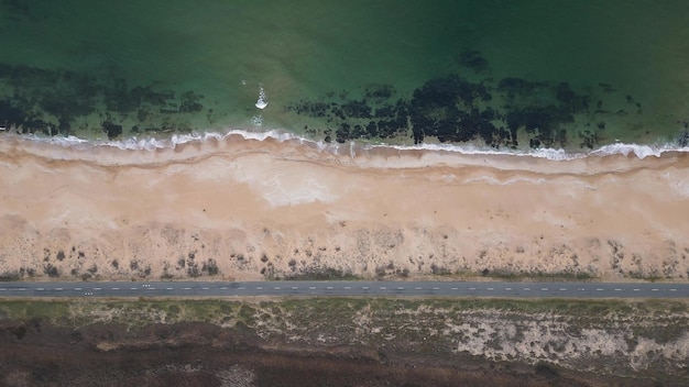 Widok drogi wzdłuż piaszczystego wybrzeża morskiego z drona lecącego nad pustą drogą i plażą