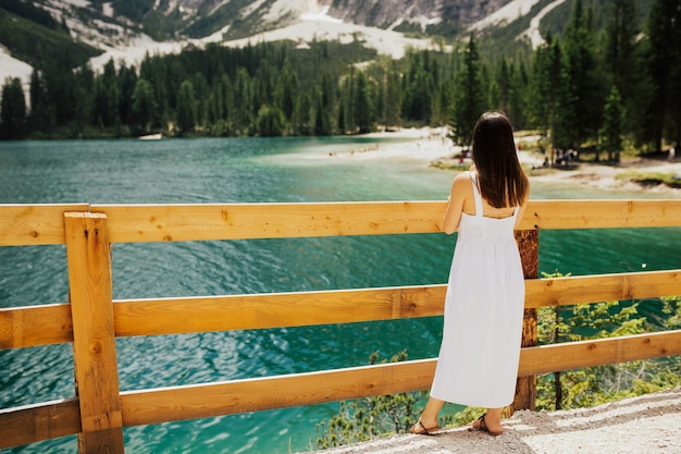 Widok dziewczyny w białej sukni z tyłu stoi w pobliżu jeziora z szmaragdową wodą.
