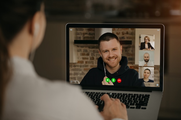 Widok Kobiety Rozmawiającej Z Partnerem Biznesowym I Kolegami W Rozmowie Wideo Na Laptopie Z Tyłu. Mężczyzna Rozmawia Ze Współpracownikami Na Konferencji Kamery Internetowej. Wieloetniczny Zespół Biznesowy O Spotkaniu Online