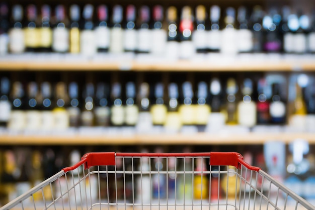 Widok koszyka na zakupy z butelkami wina na półkach z alkoholem alkoholowym w tle sklepu z winem w supermarkecie