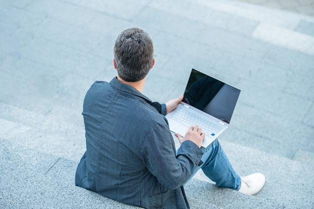 Widok mężczyzny blogującego online z laptopem na zewnątrz mężczyzna blogujący online na ulicy z tyłu