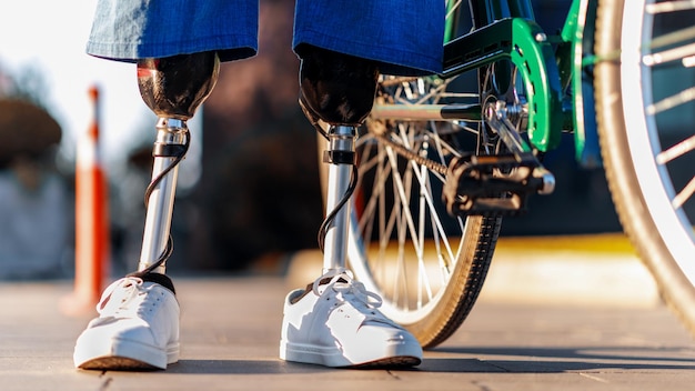Zdjęcie widok mężczyzny z protezami nóg i białymi tenisówkami stojącego obok roweru