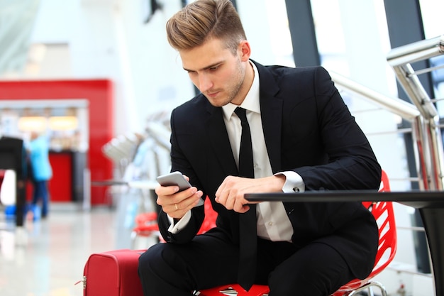 Widok młodego atrakcyjnego biznesmena za pomocą smartfona